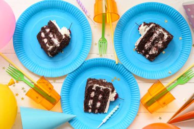 Lezzetli doğum günü pastası, fincanlar ve beyaz ahşap arka planda dekoru olan kağıt tabaklar.