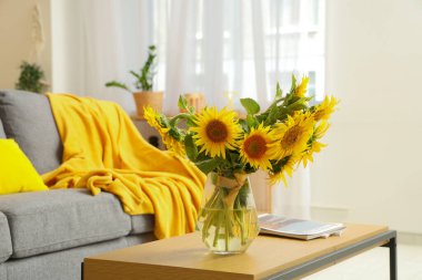 Oturma odasının iç tarafında ayçiçekleri olan rahat bir kanepe ve kahve masası.