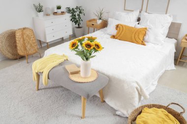 Yatak odasının içinde rahat bir yatak odası ve başucunda güzel ayçiçekleri var.