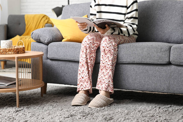 Молодая женщина в серых тапочках сидит на диване в гостиной, крупным планом