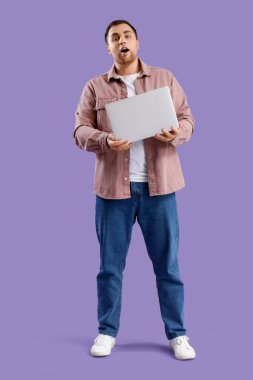 Şok olmuş genç adam menekşe arka planda dizüstü bilgisayarla