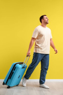 Sarı arka planda mavi bavul taşıyan mutlu genç adam. Seyahat kavramı.
