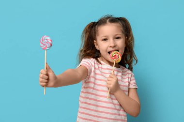 Tatlı küçük kız mavi arka planda lolipop yalıyor.
