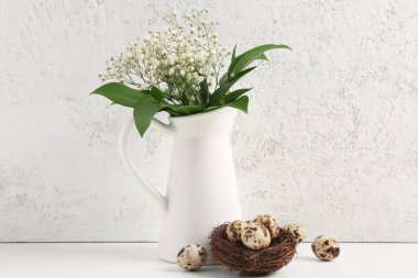 Nest with Easter eggs and gypsophila flowers in vase on table near white grunge wall