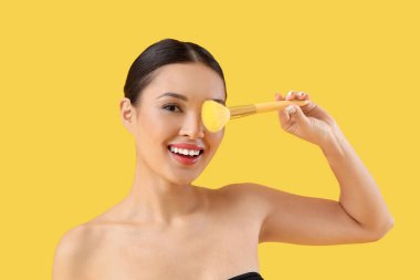 Sarı arka planda makyaj fırçası olan genç Asyalı kadın, yakın plan.