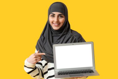 Sarı arka planda modern dizüstü bilgisayarı olan genç Müslüman kadın