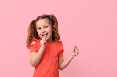 Tatlı küçük kız pembe arka planda lolipop yalıyor.