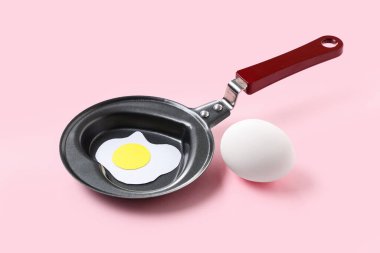 Yumurtalı kompozisyon, kalp şeklinde tava ve pembe arka planda kızarmış yumurta.