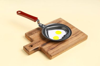 Yumurtalı kompozisyon, kalp şeklinde sahanda yumurta ve bej arka planda ahşap kesim tahtası.