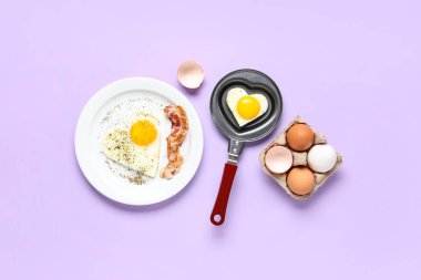 Kızartma tavasında kalp şeklinde sahanda yumurta ve leylak arkaplanda kızarmış yumurta ve pastırma kompozisyonu.