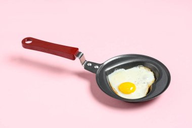 Pembe arka planda kalp şeklinde kızarmış yumurta ile kızartma tavası.