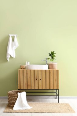 Yeşil duvarda asılı temiz havlular, lavabolu çekmeceler ve banyoda hasır çamaşır sepeti.