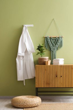 Tahta sandıktaki yumuşak havlular, beyaz bornoz ve banyodaki yeşil duvardaki makrome.