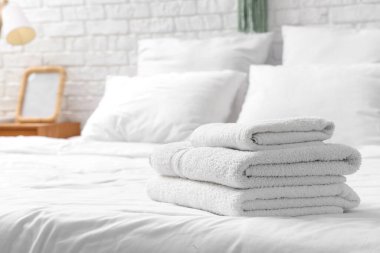 Evdeki beyaz yatağa yığılmış yumuşak havlular, yakın çekim.