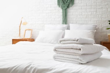 Evdeki beyaz yatağa yığılmış yumuşak havlular.