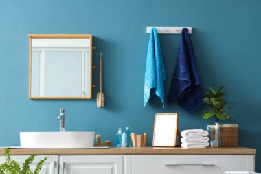 Modern banyoda mavi duvarda yumuşak havlular ve ayna asılı.