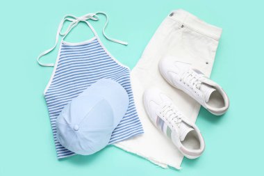 Şık beyaz spor ayakkabılar, üst, şort ve turkuaz arka planda beyzbol şapkası.