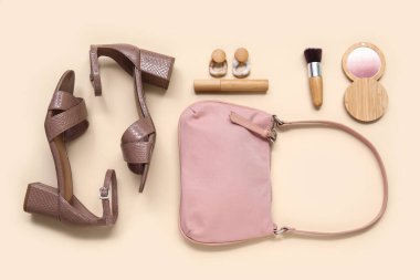 Şık topuklu sandaletler, dekoratif kozmetik ürünler ve bej arka planda aksesuarlar.