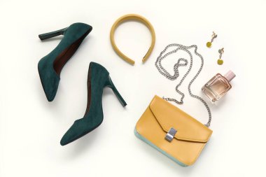 Şık topuklu ayakkabılar, çanta, saç halkası, küpeler ve beyaz arka planda bir şişe parfüm.