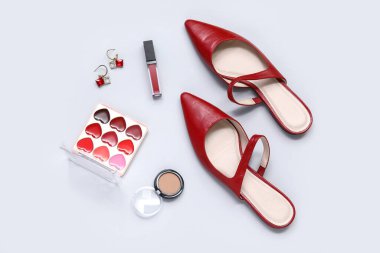 Beyaz arka planda kırmızı sapan, ruj, palet, heykeltıraş ve küpeler.