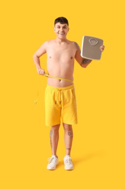 Sarı arka planda mezura ve mezura olan genç bir adam. Kilo verme konsepti