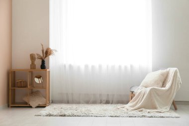 Rafa kaldırma ünitesi, halı ve sandalye. Odadaki ışık perdesinin yanında ekoseli ve yastıklı.