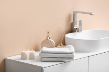 Banyodaki bej duvarın yanındaki masada bir yığın temiz havlu ve mum var.