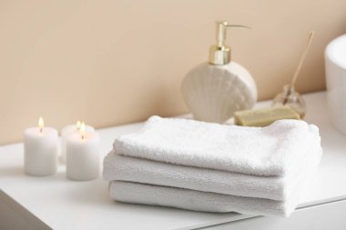 Banyodaki bej duvarın yanındaki masada temiz havlu ve mum yığını var.