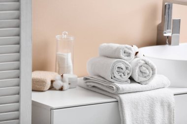 Temiz yumuşak havlular, pamuklu tutucu ve pamuklu çiçekler banyoda bej duvarın yanındaki masada.