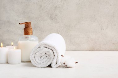 Temiz yumuşak havlu, bir şişe kozmetik ürünü ve banyodaki grunge duvarının yanında mumlar.