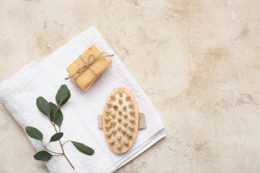 Temiz havlu, vücut masajı fırçası, sabun çubukları ve arkaplanda bitki.