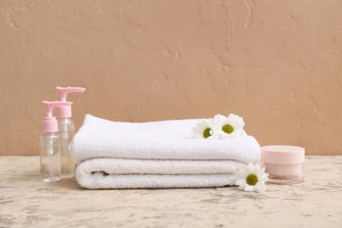 Temiz yumuşak havlular, kozmetik ürünler ve kahverengi duvarın yanındaki çiçeklerle kompozisyon