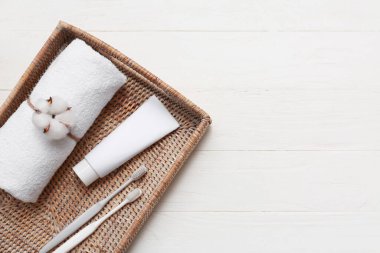 Hasır sepetli güzel kompozisyon, yumuşak havlu, ağız bakım seti ve beyaz ahşap arka planda pamuk çiçeği, yakın plan.