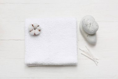Temiz yumuşak havlu, pamuk tomurcukları ve beyaz ahşap arka planda spa taşlarıyla güzel bir kompozisyon.