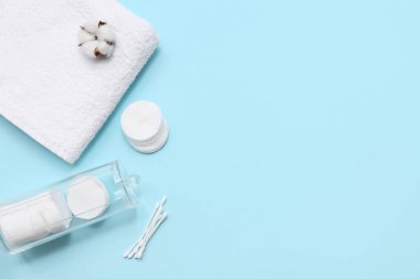 Temiz yumuşak havlu, pamuk pedleri, cam tutacağı, pamuk tomurcukları ve mavi arka planda pamuk çiçeği olan kompozisyon
