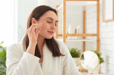 Güzel genç bir kadın banyoda pamuk tomurcuğuyla makyaj yapıyor.