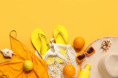Parmak arası terlik, mayo, güneş gözlüğü ve sarı arka planda hasır şapka.