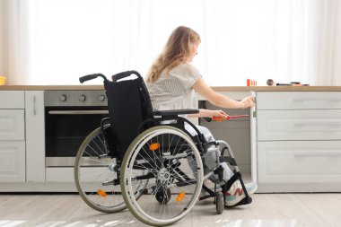 Tekerlekli sandalyedeki genç kadın evde tornavidayla çekmeceyi tamir ediyor.