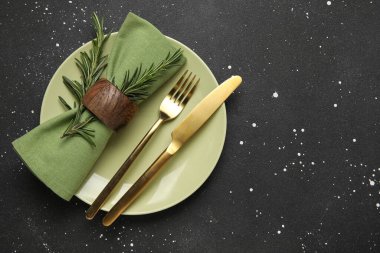 Siyah grunge arkaplan üzerinde peçete, çatal bıçak ve biberiye ile şık masa ayarları