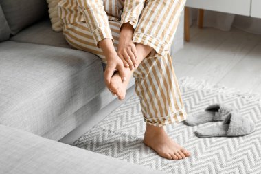 Evde eklem ağrısı çeken pijamalı genç bir kadın.