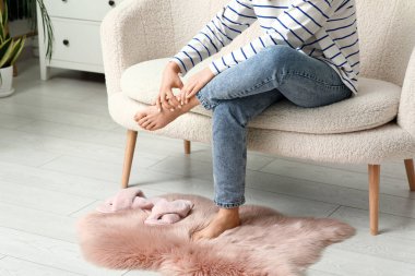 Evde eklem ağrısı çeken kot pantolonlu genç bir kadın.