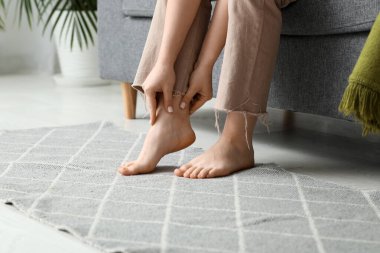 Oturma odasındaki rahat koltukta eklem ağrısı çeken genç bir kadın.