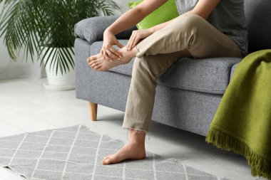 Oturma odasındaki rahat koltukta eklem ağrısı çeken genç bir kadın.