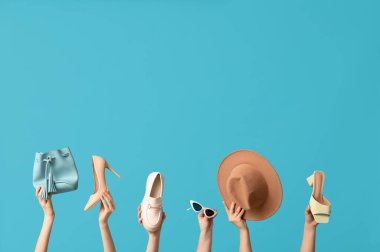 Şapkalı, güneş gözlüklü, çantalı ve mavi arka planda farklı ayakkabılı kadın elleri.