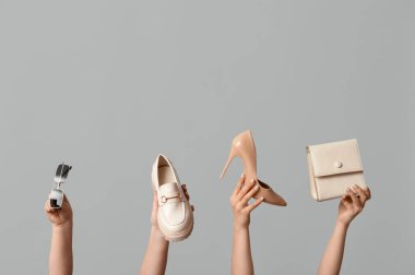 Çantası, güneş gözlüğü ve gri arka planda farklı ayakkabıları olan kadın elleri.