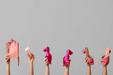 Çantası, güneş gözlüğü ve gri arka planda topuklu ayakkabısı olan kadın elleri.