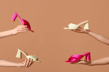 Bej arka planda farklı topuklu sandaletleri olan kadın elleri.