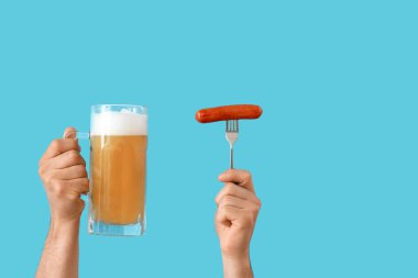 Mavi arka planda bira bardağı ve sosis tutan eller