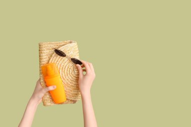 Yeşil arka planda çanta, güneş gözlüğü ve güneş kremi olan kadın elleri