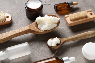 Gri arka planda kozmetik yağ ve masaj fırçalarıyla dolu kaşık dolusu Shea yağı.
